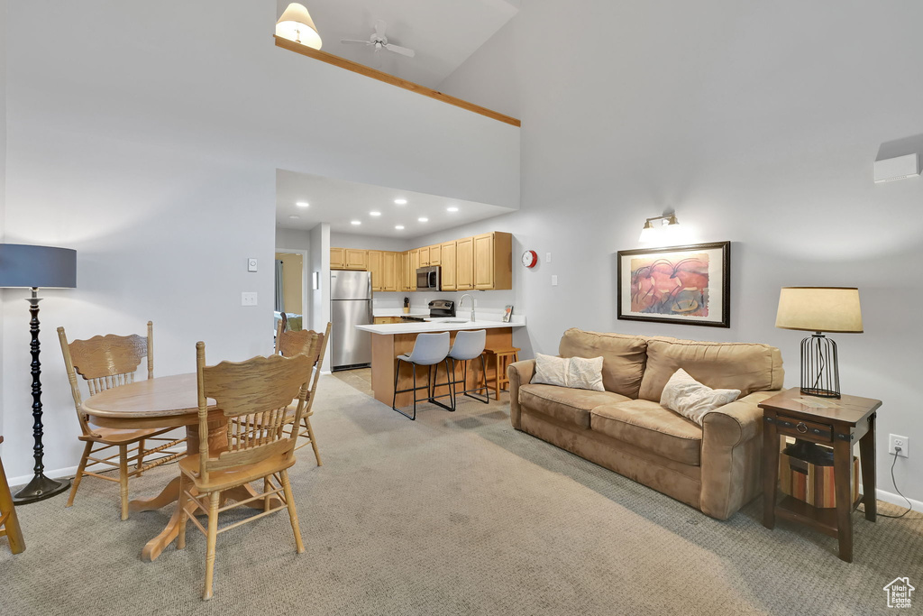 Living area featuring baseboards, light carpet, a ceiling fan, recessed lighting, and a high ceiling