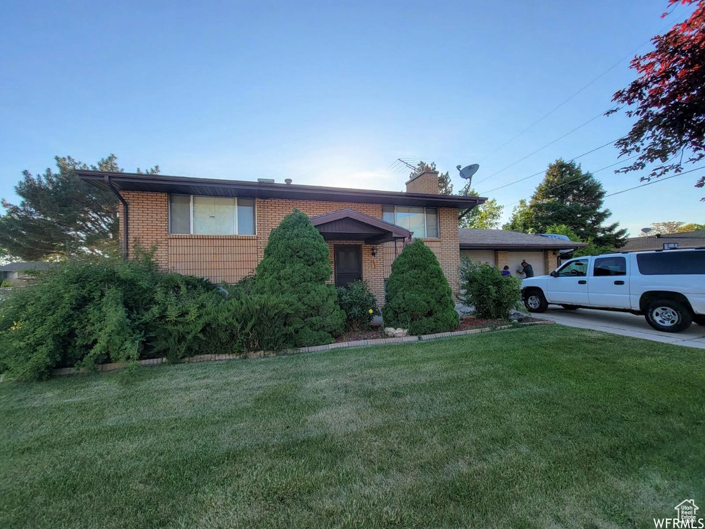 View of front of home with brick siding, a front lawn, a chimney, and an attached garage