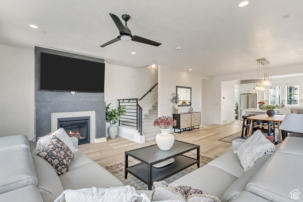 Living room featuring a glass covered fireplace, stairs, light wood finished floors, a ceiling fan, and recessed lighting