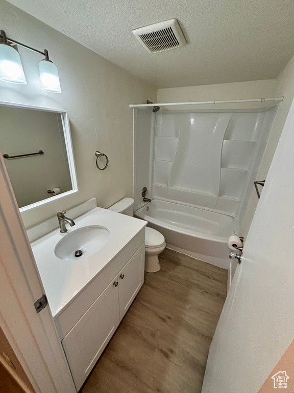 Full bath featuring wood finished floors, toilet, a textured ceiling, vanity, and  shower combination