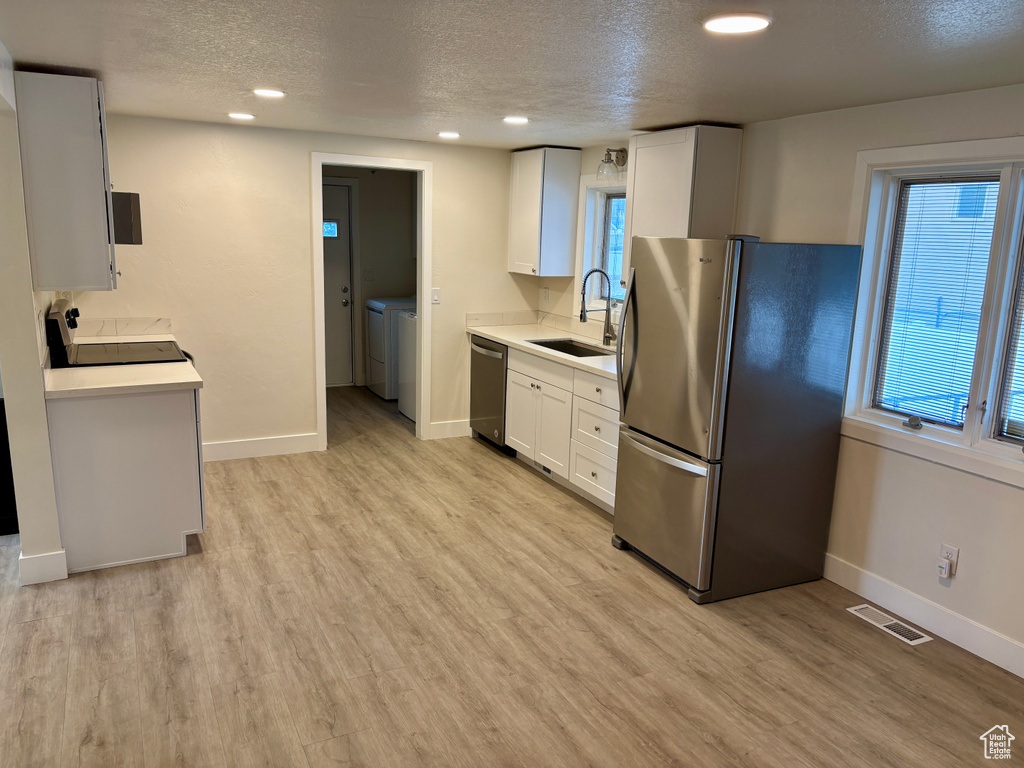 Kitchen with appliances with stainless steel finishes, a sink, separate washer and dryer, a textured ceiling, and baseboards