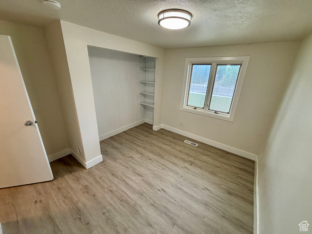 Unfurnished bedroom featuring a textured ceiling, baseboards, light wood-style flooring, and a closet