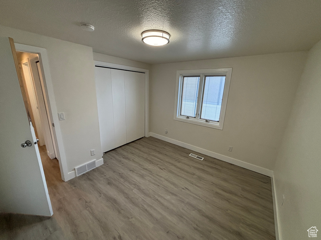 Unfurnished bedroom featuring baseboards, wood finished floors, a textured ceiling, and a closet