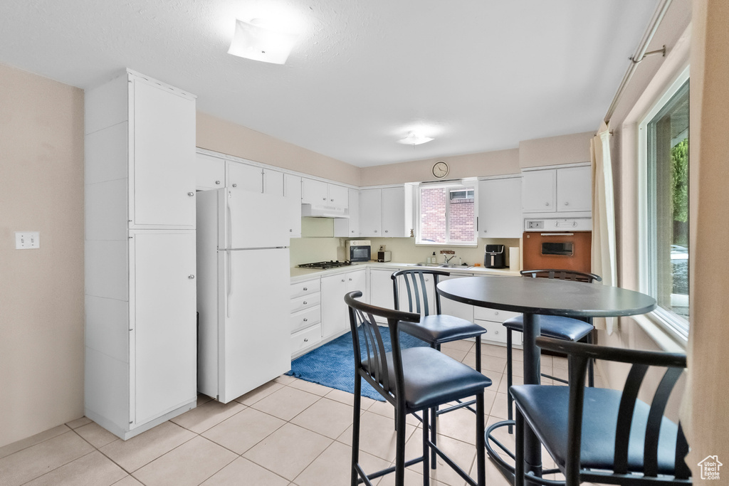 Kitchen with freestanding refrigerator, oven, white cabinets, and light tile patterned floors