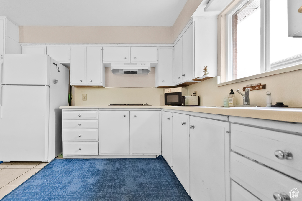Kitchen featuring freestanding refrigerator, light countertops, white cabinetry, under cabinet range hood, and stovetop