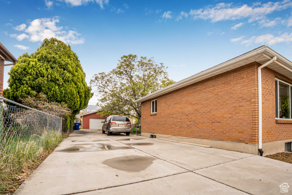 View of side of property featuring fence, a detached garage, an outbuilding, and brick siding