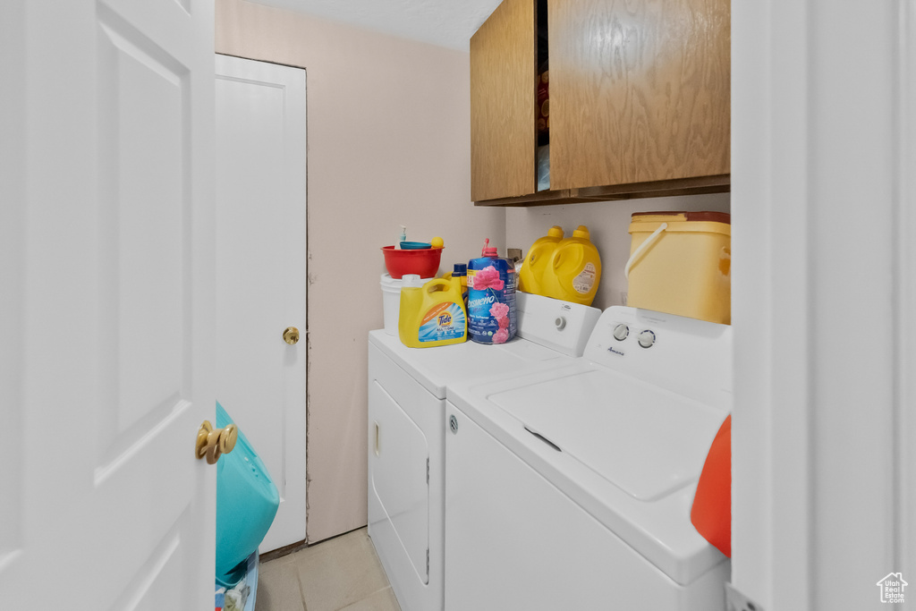 Clothes washing area with cabinet space, light tile patterned floors, and washing machine and dryer