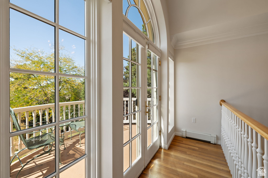 Doorway to outside featuring a baseboard radiator, ornamental molding, baseboards, and wood finished floors