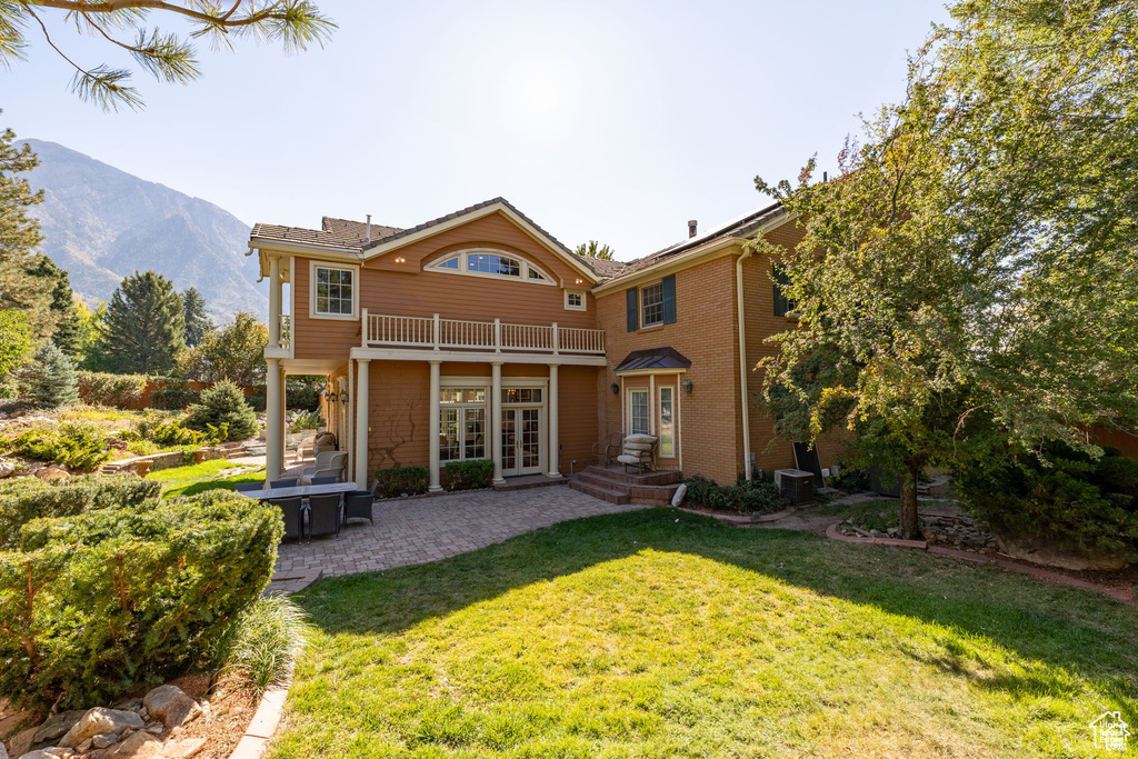 Rear view of property with french doors, a balcony, a lawn, a patio area, and a mountain view