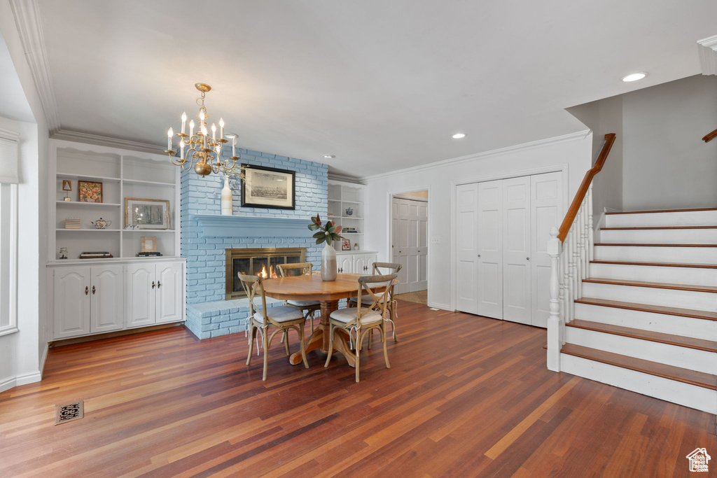 Dining room with wood finished floors, stairway, a brick fireplace, a chandelier, and ornamental molding