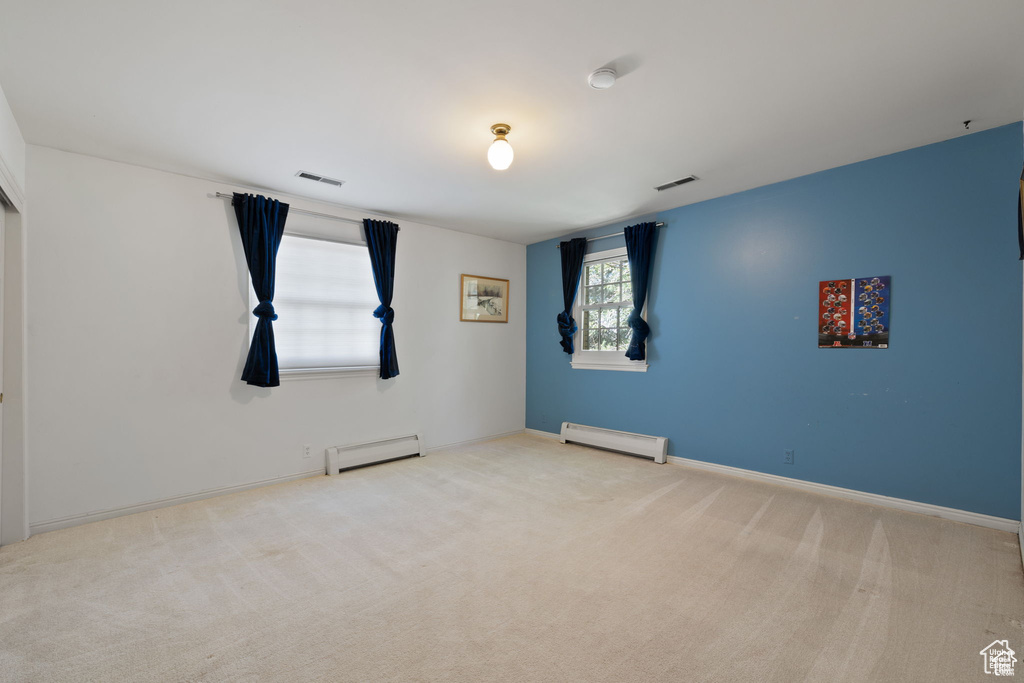 Carpeted empty room featuring a baseboard heating unit, baseboards, and a smoke detector