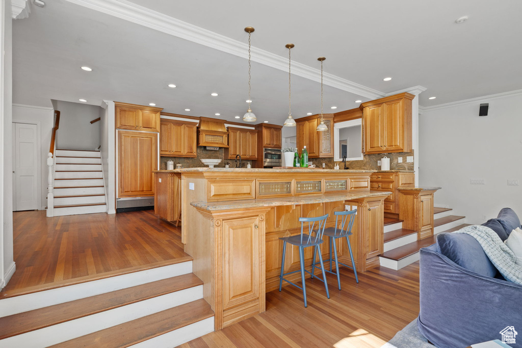Kitchen featuring light wood finished floors, open floor plan, decorative backsplash, crown molding, and recessed lighting