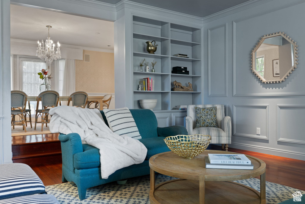 Living area with a chandelier, a decorative wall, crown molding, wood finished floors, and built in features
