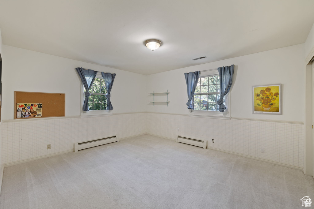 Carpeted empty room with a baseboard heating unit, a wainscoted wall, and plenty of natural light