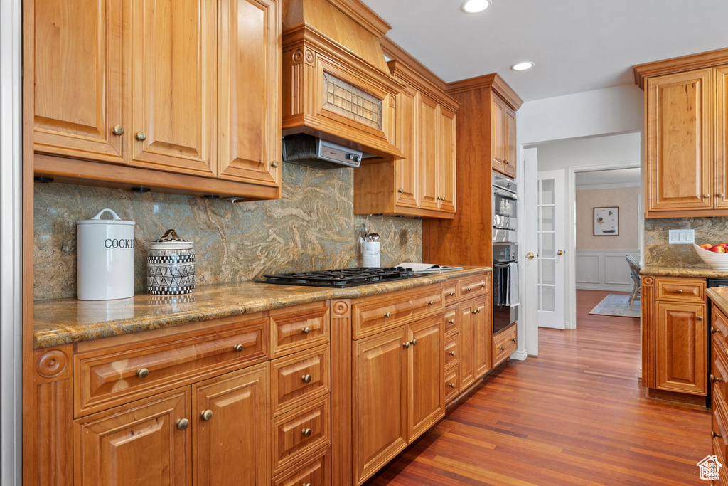 Kitchen featuring black gas cooktop, dark wood-style flooring, a wainscoted wall, custom range hood, and recessed lighting