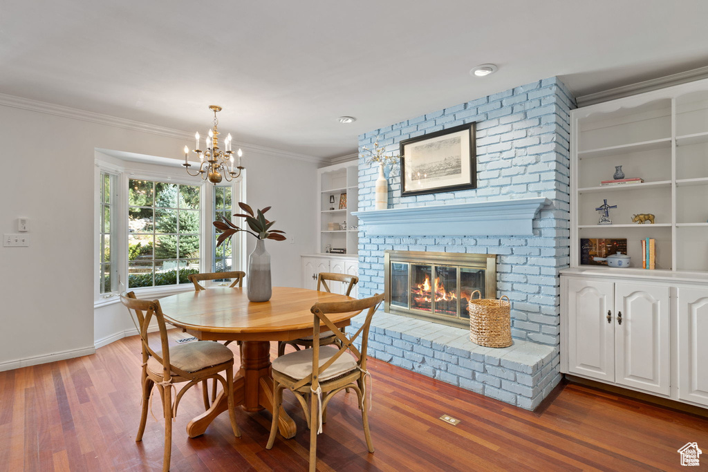 Dining space with wood finished floors, a chandelier, a brick fireplace, built in features, and crown molding