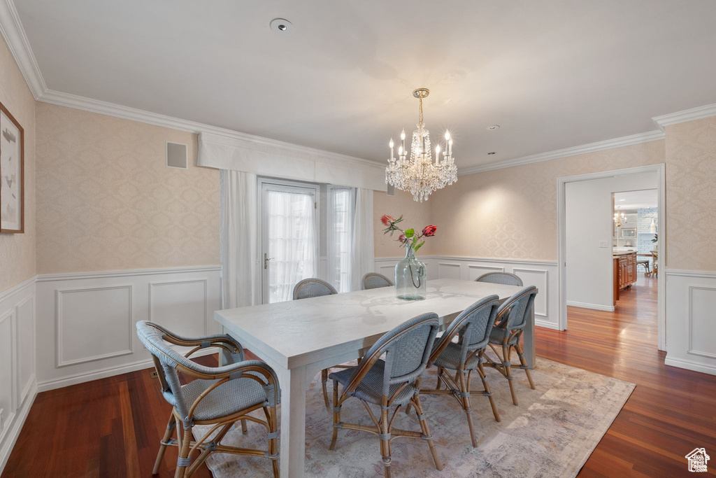 Dining room featuring a chandelier, wood finished floors, wainscoting, crown molding, and a decorative wall