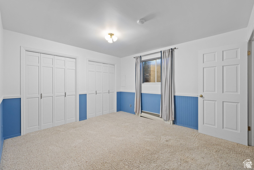 Unfurnished bedroom featuring two closets, carpet floors, and wainscoting