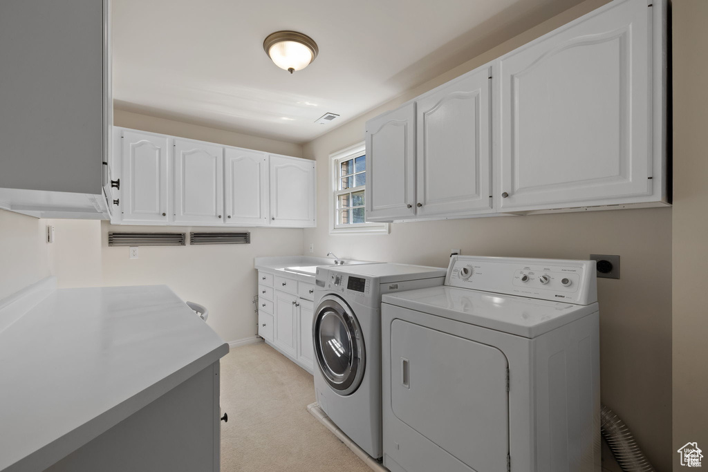 Laundry room featuring cabinet space, washing machine and clothes dryer, light carpet, and baseboards