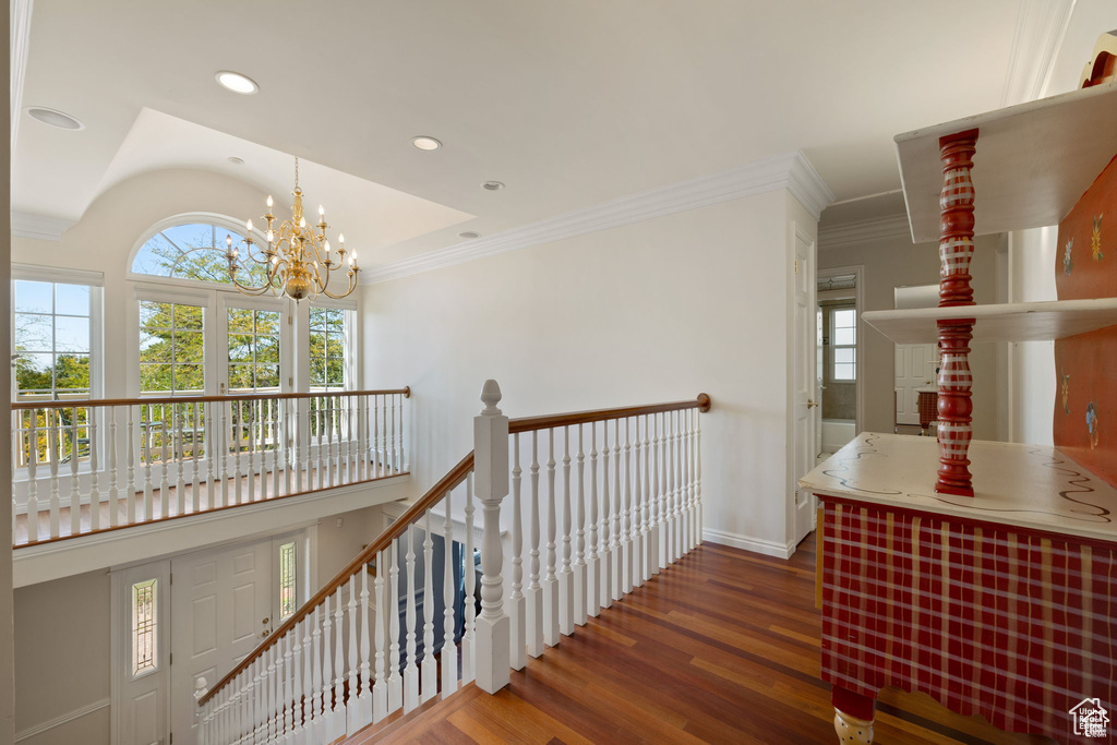 Hall with healthy amount of natural light, an upstairs landing, wood finished floors, a chandelier, and crown molding