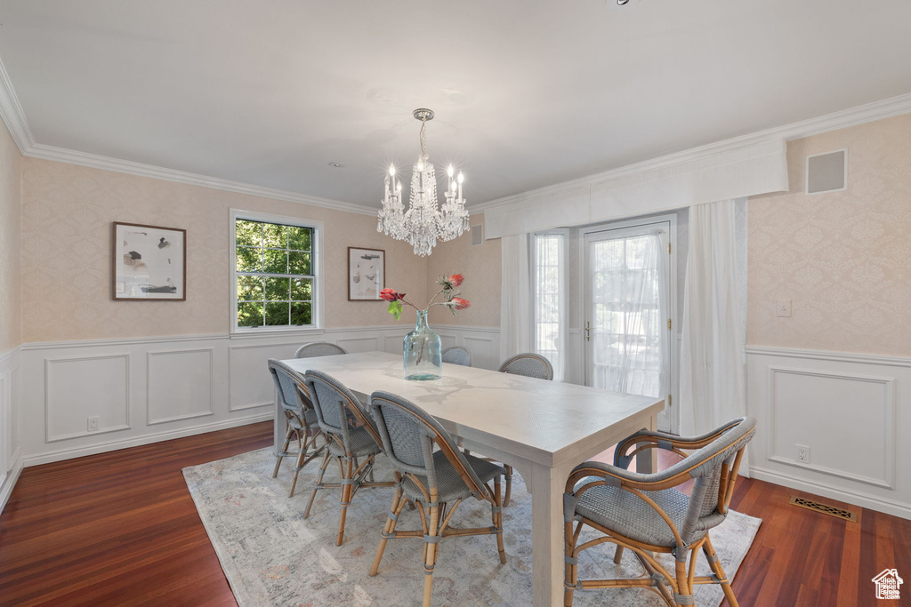 Dining area featuring ornamental molding, a chandelier, dark wood-style flooring, wallpapered walls, and wainscoting