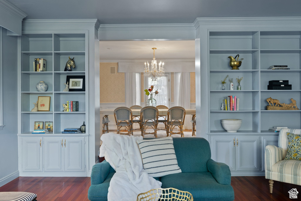 Sitting room with a chandelier, dark wood-style floors, crown molding, and built in shelves