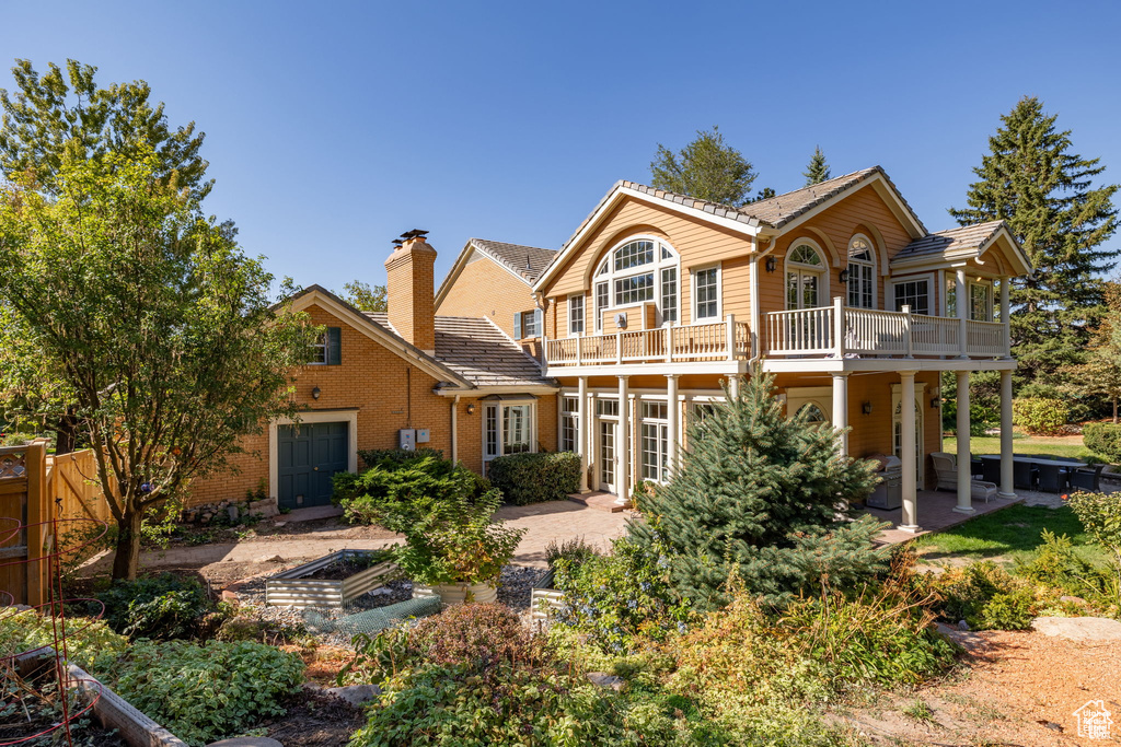 Back of property featuring a garden, a balcony, a patio area, and brick siding