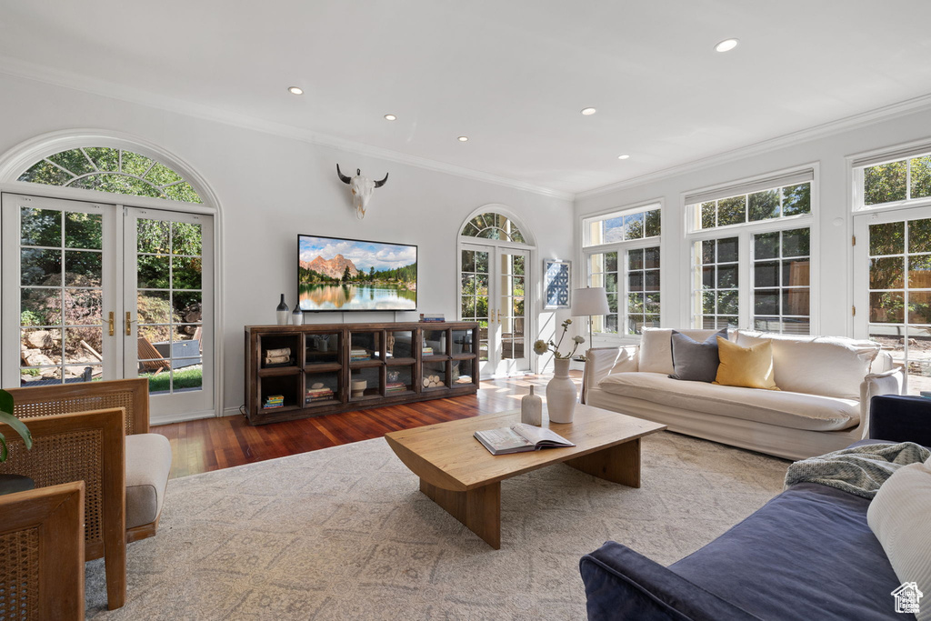 Living area with french doors, crown molding, wood finished floors, plenty of natural light, and recessed lighting