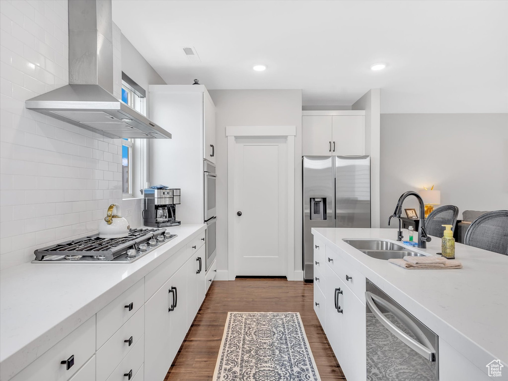 Kitchen featuring wall chimney range hood, a sink, stainless steel appliances, backsplash, and dark wood-style floors