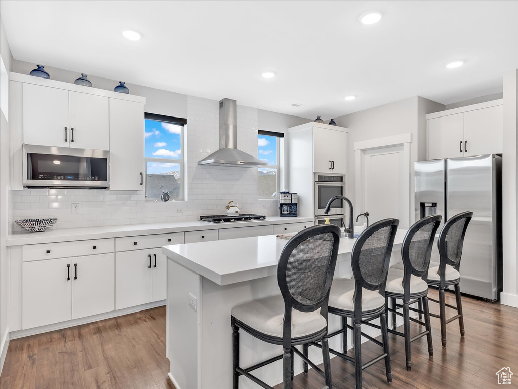 Kitchen with stainless steel appliances, wall chimney range hood, a breakfast bar, tasteful backsplash, and light countertops