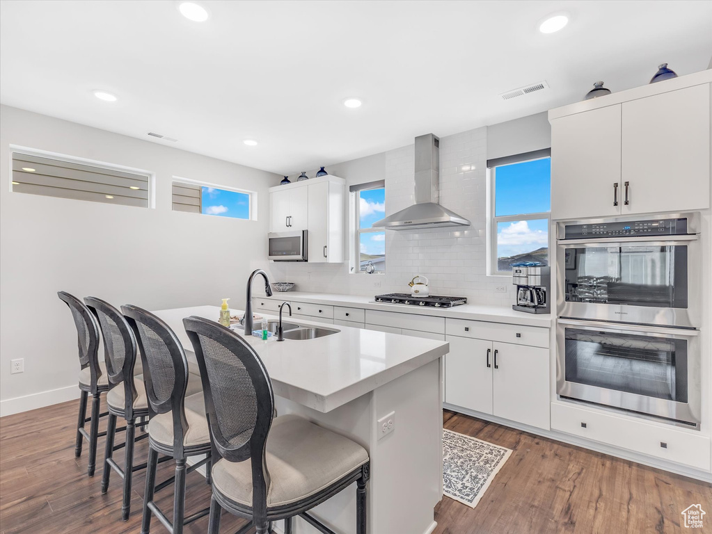 Kitchen featuring wall chimney range hood, stainless steel appliances, a sink, a breakfast bar area, and recessed lighting