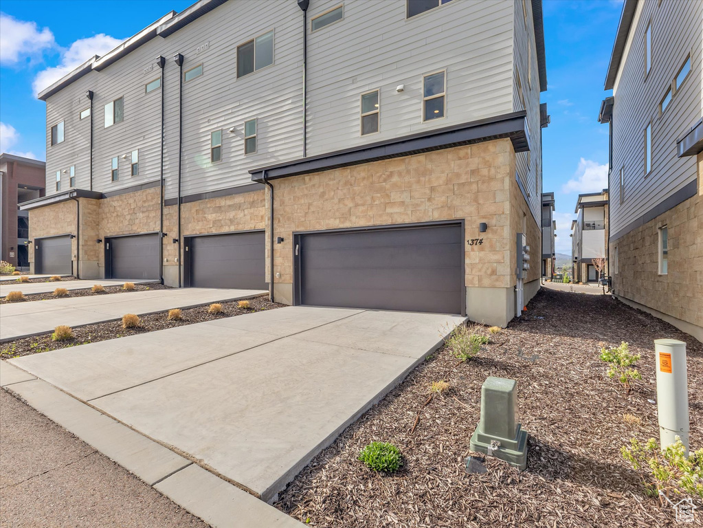 Rear view of property featuring a garage, concrete driveway, and stone siding