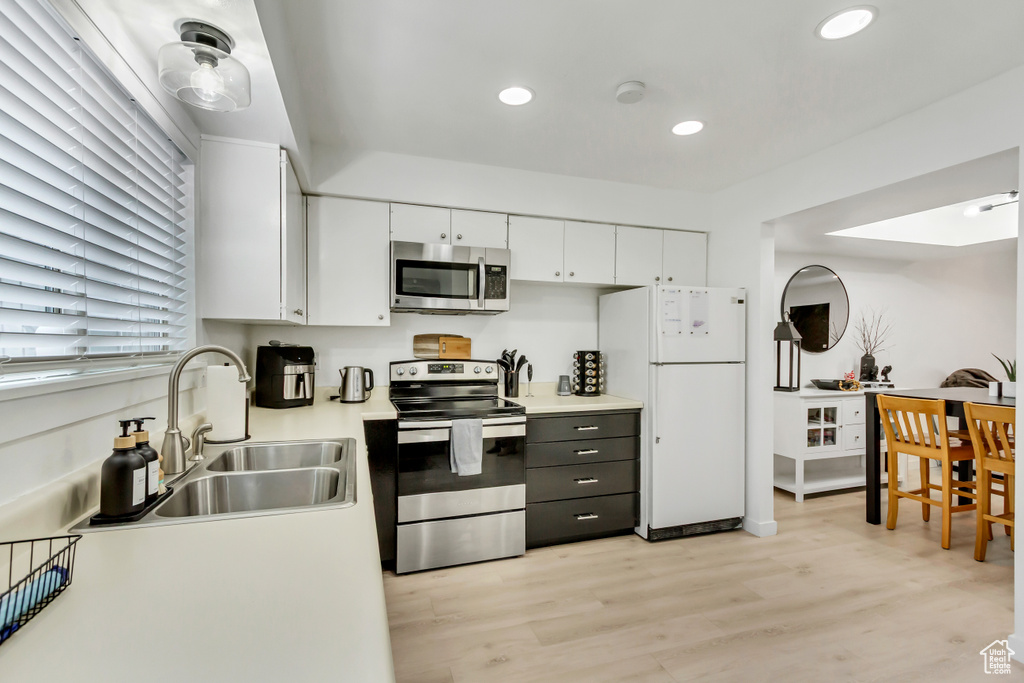 Kitchen featuring appliances with stainless steel finishes, a sink, white cabinetry, light countertops, and light wood-style flooring