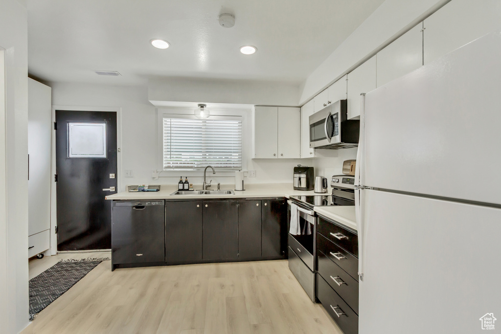 Kitchen with appliances with stainless steel finishes, a sink, white cabinetry, light wood-style floors, and recessed lighting