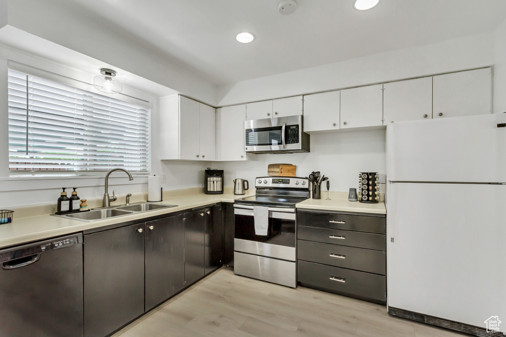 Kitchen with stainless steel appliances, a sink, white cabinetry, light wood-type flooring, and light countertops