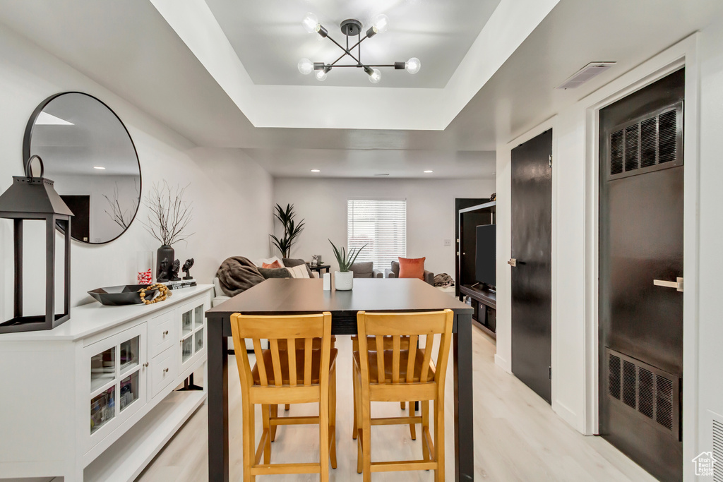Dining area with a chandelier, light wood-type flooring, a raised ceiling, a heating unit, and recessed lighting