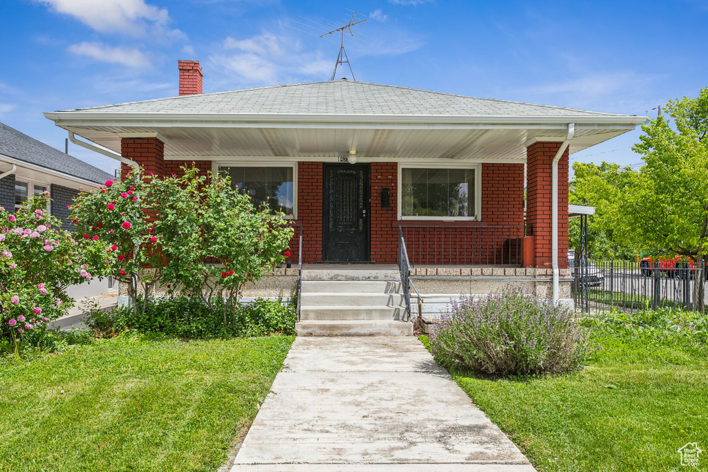 Bungalow-style home featuring covered porch, a chimney, and brick siding