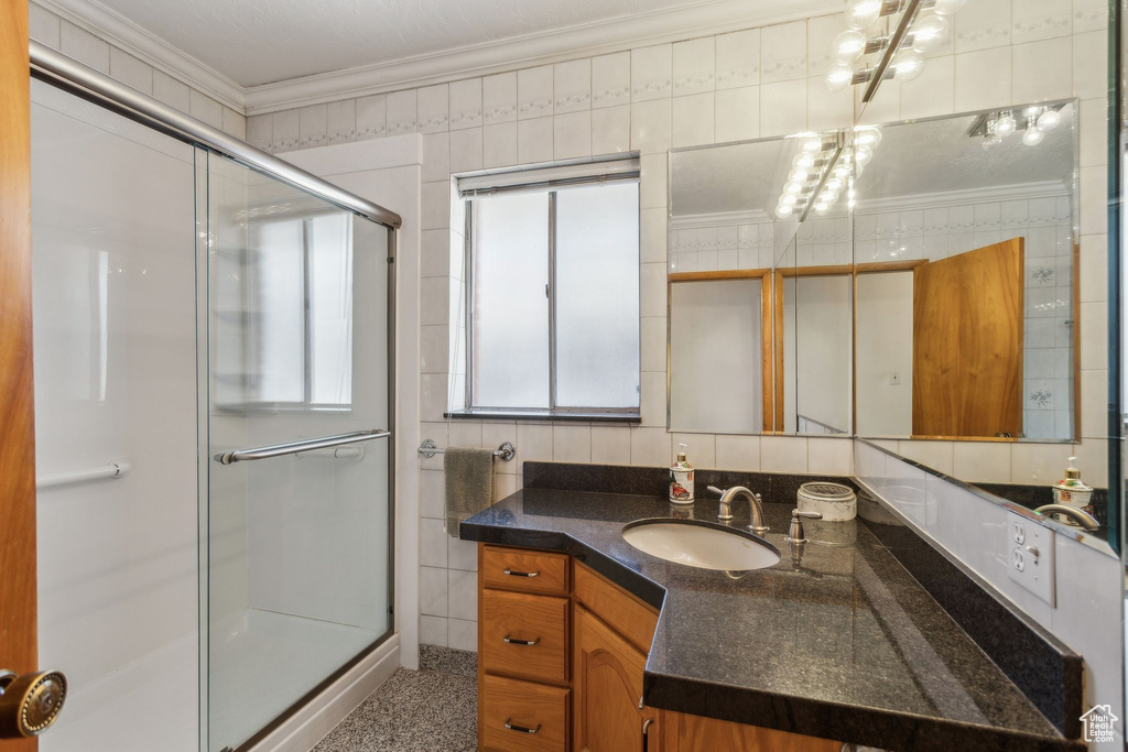 Bathroom featuring a shower stall, ornamental molding, vanity, and tile walls
