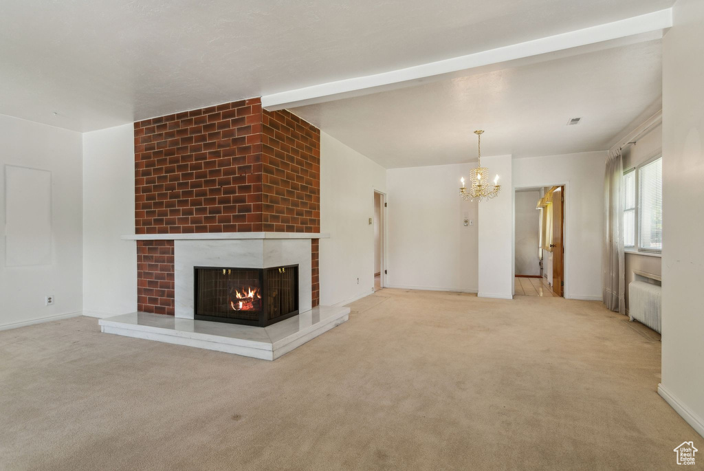 Unfurnished living room with a chandelier, radiator heating unit, a fireplace, carpet floors, and beamed ceiling