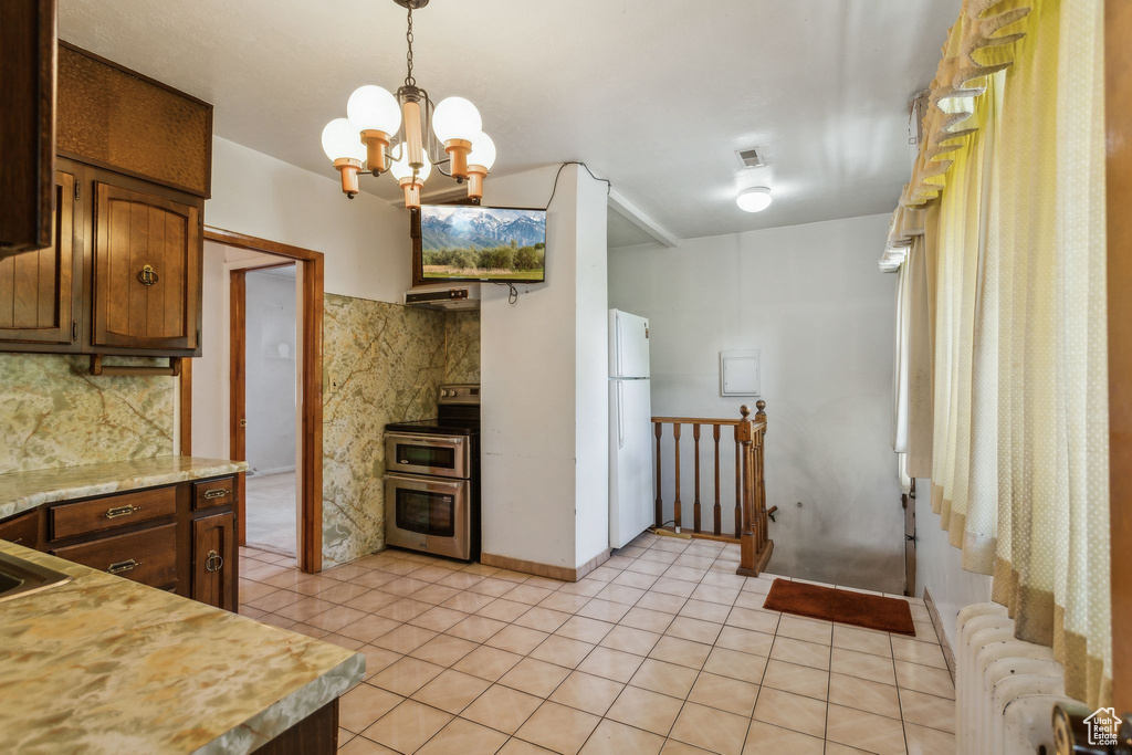 Kitchen with double oven range, freestanding refrigerator, light countertops, radiator, and a chandelier
