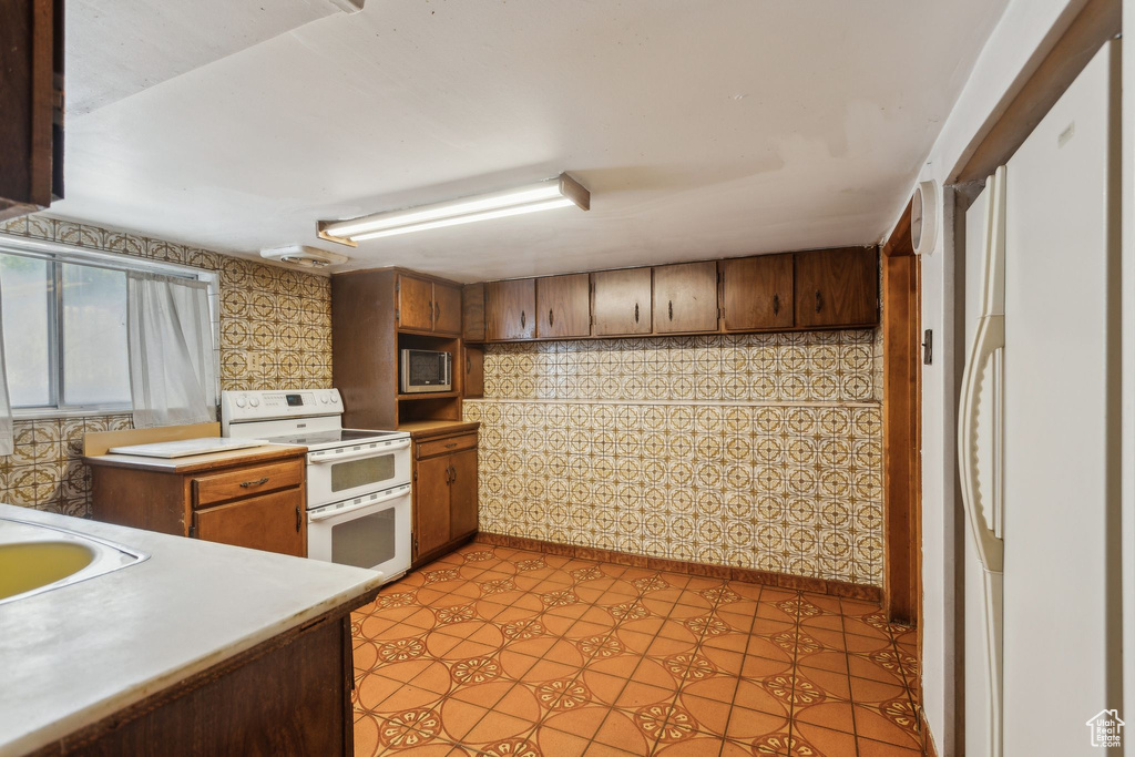 Kitchen featuring range with two ovens, stainless steel microwave, light countertops, and brown cabinetry
