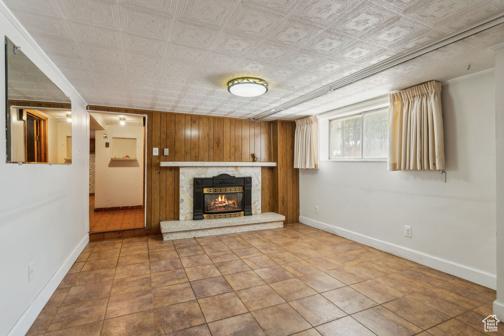 Unfurnished living room with a glass covered fireplace, baseboards, wooden walls, an ornate ceiling, and crown molding