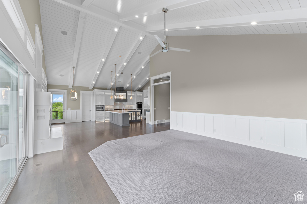 Living area featuring high vaulted ceiling, dark wood finished floors, a ceiling fan, beamed ceiling, and a wainscoted wall