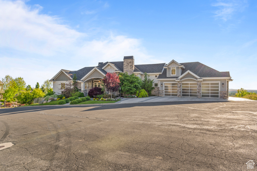 View of front facade featuring stone siding, asphalt driveway, a garage, and a chimney