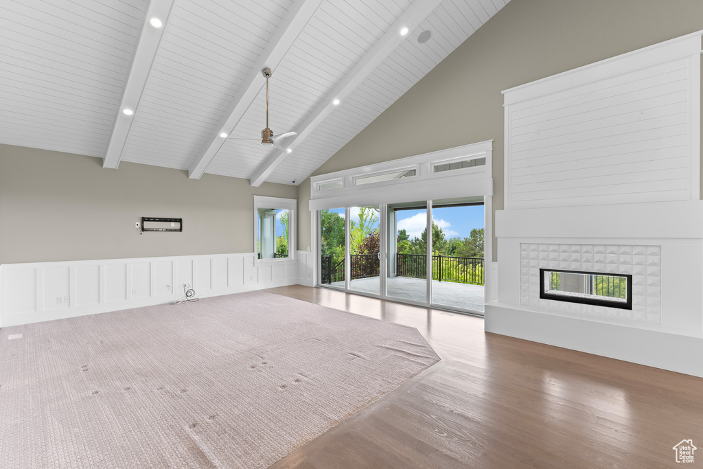 Unfurnished living room featuring high vaulted ceiling, a tiled fireplace, wood finished floors, beamed ceiling, and a ceiling fan