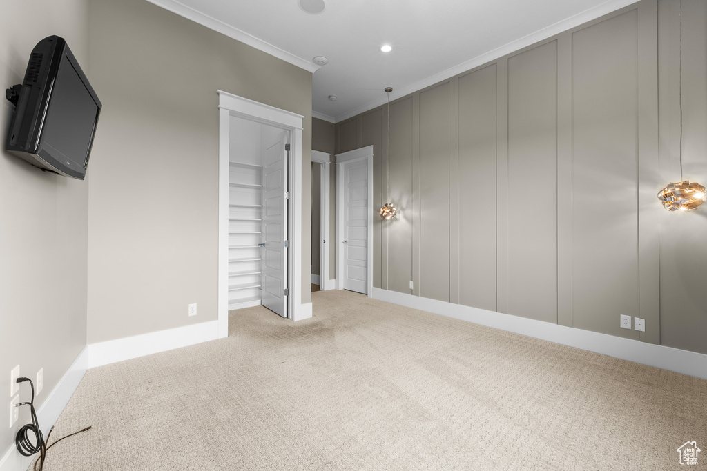 Unfurnished bedroom with carpet floors, baseboards, a spacious closet, ornamental molding, and a decorative wall