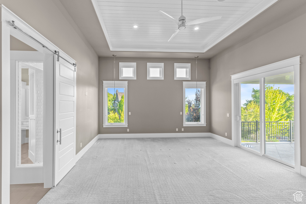Empty room featuring a barn door, baseboards, ceiling fan, and healthy amount of natural light