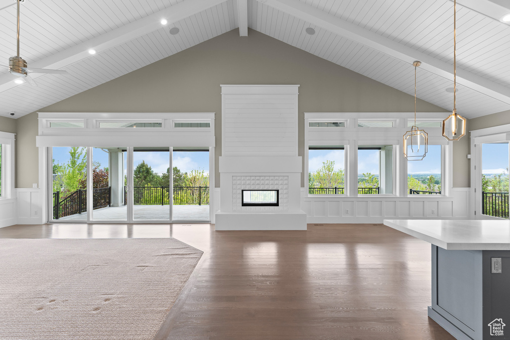 Unfurnished living room with wood finished floors, high vaulted ceiling, beamed ceiling, a decorative wall, and a glass covered fireplace
