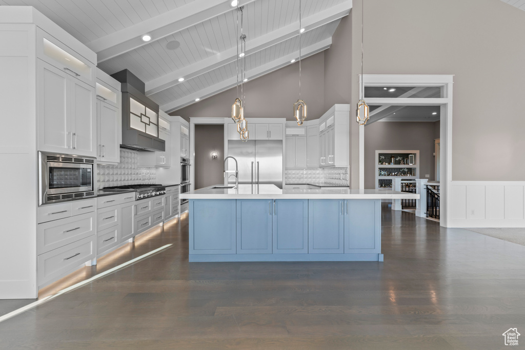 Kitchen featuring built in appliances, a sink, beamed ceiling, white cabinetry, and backsplash