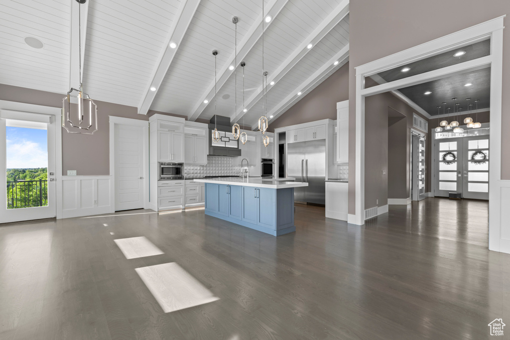 Kitchen with built in appliances, light countertops, dark wood-style flooring, white cabinetry, and high vaulted ceiling